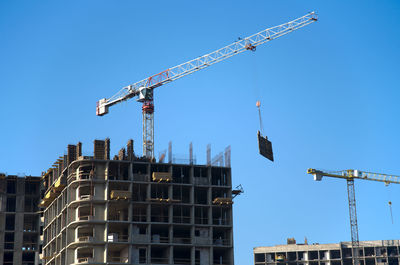 Low angle view of cranes at construction site against sky