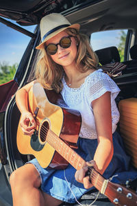 Portrait of smiling young woman playing guitar in car 