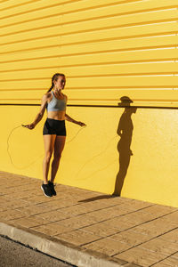 Full length of woman standing on footpath against yellow wall