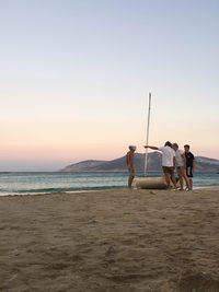 People on beach against clear sky during sunset