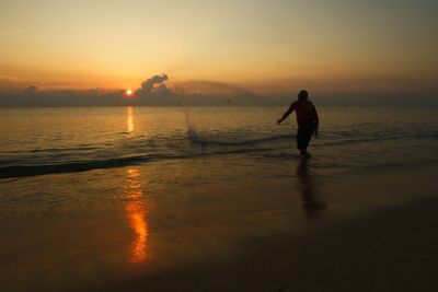 Silhouette man standing on beach against sky during sunset