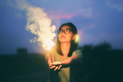 Young woman holding sparklers while outdoors at dusk