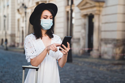 Woman wearing mask using smart phone standing on road