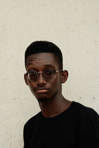 Portrait of young man wearing eyeglasses standing against wall