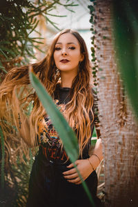 Portrait of young woman wearing hat standing against plants