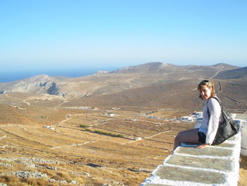Young woman sitting on mountain against clear blue sky