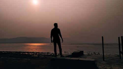 Rear view of silhouette man standing on beach during sunset