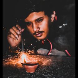 Portrait of young man holding fire in the dark