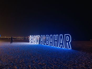 Man standing by illuminated text on beach against sky at night