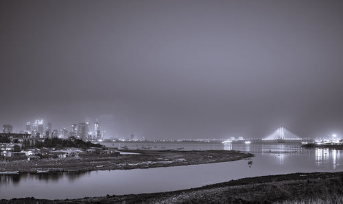 Illuminated city by sea against sky at night