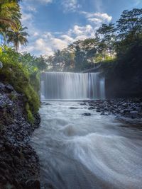 Scenic view of waterfall in forest against sky