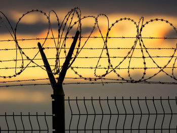 Barbed wire fence against sky during sunset