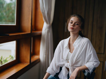 Portrait of young woman standing by window at home