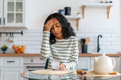 African-american female dealing with headache. dissolving pill in glass of water in kitchen