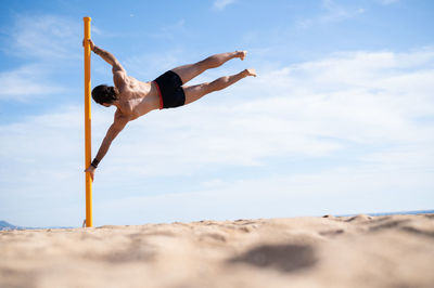 Low angle view of man jumping on sand at beach against sky