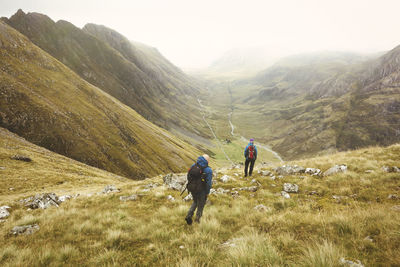 Rear view of people walking on mountain against sky