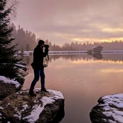 Full length of man standing on lake against sky during sunset