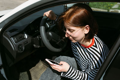 Portrait of a young brunette woman driving in a car using a smartphone