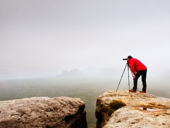 Man photographing rock on mountain against sky