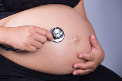 Midsection of pregnant woman holding stethoscope against gray background