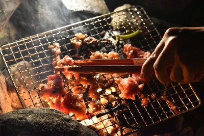 Person holding meat on barbecue grill