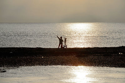 Silhouette people standing on beach against sky during sunset