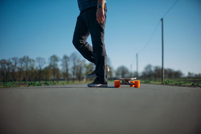 Low section of man skateboarding on road against clear sky