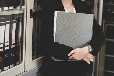 Midsection of businesswoman with file standing in office