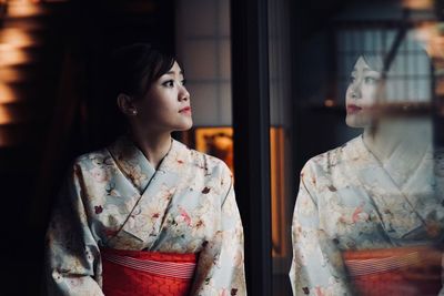 Thoughtful woman wearing traditional clothing looking through window at home