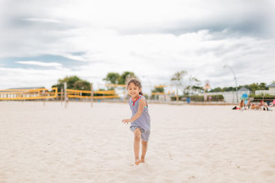 Portrait of young woman standing at beach against sky