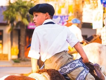 Rear view of boy riding horse in city