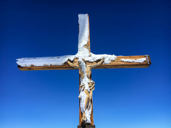 Snow covered cross with a wooden figure of jesus christ at peak of klein matterhorn against blue sky
