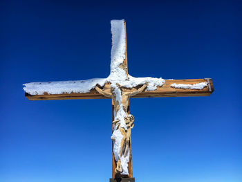 Low angle view of cross sculpture against blue sky