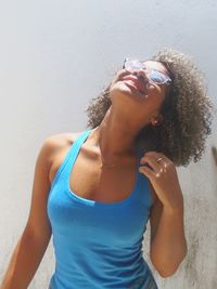 Happy young woman standing against wall on sunny day