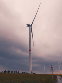 Low angle view of wind turbines on field against sky