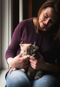 Woman looking at two adorable kittens that she is holding in her lap.