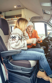 Women with a coffee looking mobile sitting in the front seat of a camper van