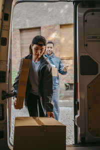 Male and female delivery coworkers unloading boxes from van trunk