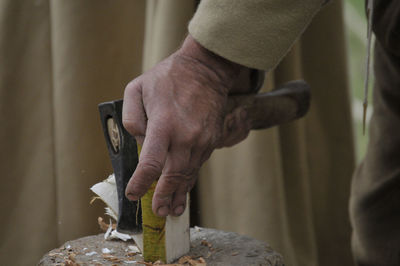 Midsection of carpenter cutting wood on tree stump