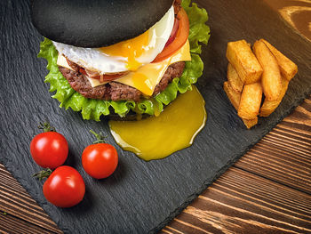 Black burger with an egg on a stone plate. cherry tomatoes. fried potatoes.