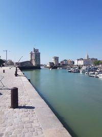 Buildings by river against clear blue sky