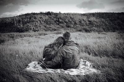 Rear view of couple embracing while sitting on blanket at grassy field