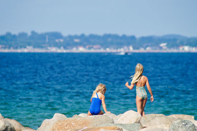 Rear view of women walking on rocks at sea shore against sky