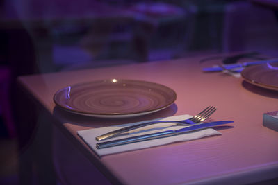 Close-up of a light purple plate with fork and knife on a purple tablet 