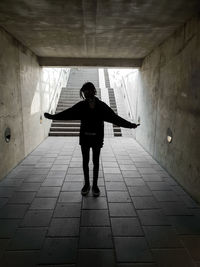 Full length of silhouette man with arms outstretched standing in tunnel