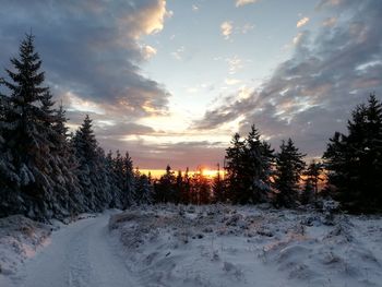 Snow covered land against sky during sunset