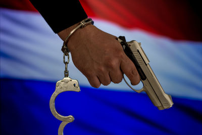 Cropped hand with handcuffs holding gun against dutch flag