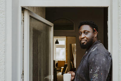 Side view portrait male carpenter holding coffee cup at doorway of house