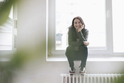 Portrait of smiling woman sitting on window sill in a loft