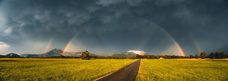 Panoramic image of glowing double rainbow above fields and road in salzburg, austria